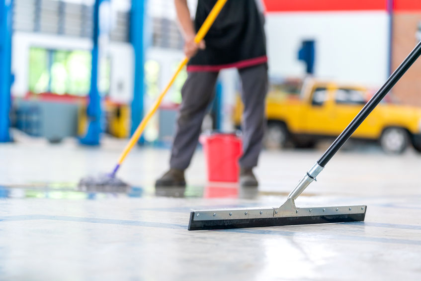 Select the focus mop, service staff man using a mop to remove water in the uniform cleaning the protective clothing of the new epoxy floor in an empty warehouse or car service center.